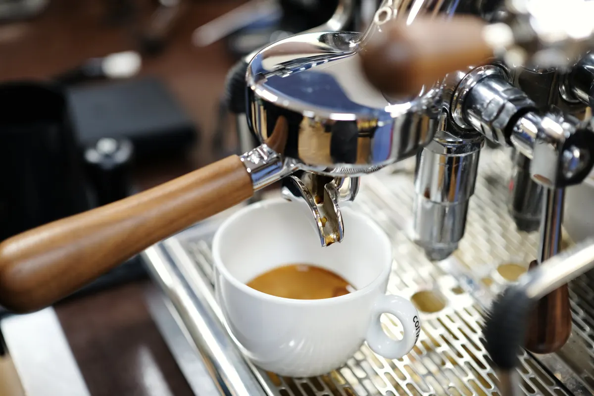 Espresso läuft aus dem Siebträger mit Holzgriff in eine weiße Tasse